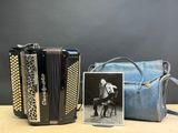 une vieille photo d'une femme jouant de l'accordéon à côté d'un sac à main bleu