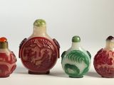 Quatre petites flacons à tabac chinois en verre sont alignés sur une surface blanche