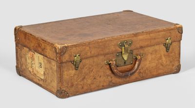 une vieille valise posée par terre, sur laquelle est accrochée une étiquette