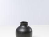 un vase noir posé sur une table blanche, avec un mur blanc en arrière-plan