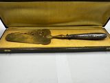 un couteau ancien à manche en laiton, présenté dans un étui posé sur une surface blanche