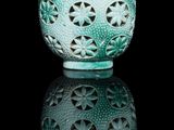 un vase vert avec un couvercle rouge posé sur une surface noire