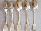 cinq cuillères en argent et une fourchette sont alignées sur une table