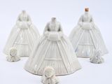 three white ceramic figurines of dresses and a teddy bear on a white background