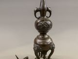 a small bronze vase on a stand next to a screw