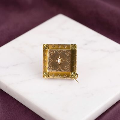 une petite horloge carrée en or posée sur un socle en marbre