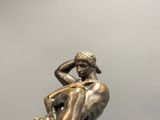 bronze statue of a man sitting on a rock with his hands on his head