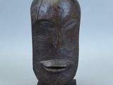 un gros plan sur une sculpture en bois représentant un visage, posée sur un socle