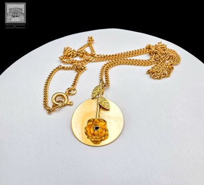 collier plaqué or avec un pendentif en forme de rose dorée et une chaîne dorée sur un fond blanc