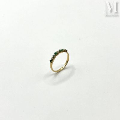 a close up of a gold ring with green stones on a white surface