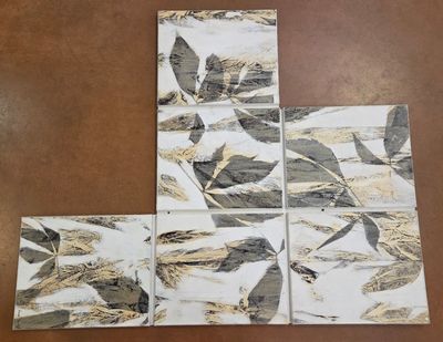 four coasters with gold and black leaves on them sitting on a table