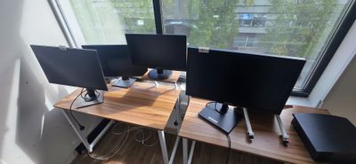 three computer monitors sitting on a desk in front of a window