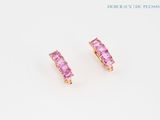 une paire de boucles d'oreilles en saphir rose posées sur une surface blanche
