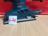 un gros plan d'une ponceuse orbitale Bosch posée sur une table en bois