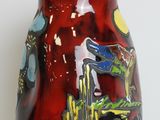 a red vase with a painting on it sitting on a table