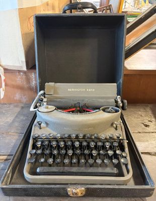 une vieille machine à écrire posée dans un coffret, par terre