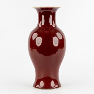 un vase rouge posé sur une surface blanche