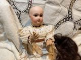 a doll that is sitting next to a doll that is laying on a bed