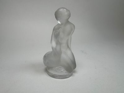 une figurine en verre représentant une femme assise sur une surface blanche