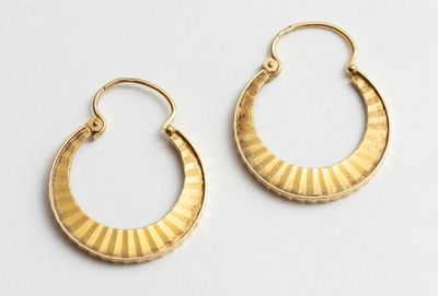une paire de boucles d'oreilles en or posées sur une surface blanche