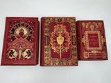 Trois livres sont alignés sur une surface blanche ; l'un est rouge et l'autre est doré.