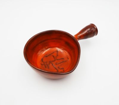 a small red bowl with a wooden handle on a white surface
