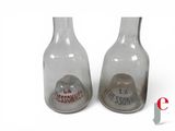 two glass bottles with sand inside of them on a white surface
