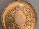 a gold pocket watch on a table with a gray background