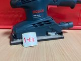 une ponceuse orbitale Bosch posée sur une table, à côté d'une boîte rouge