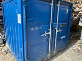 un conteneur bleu posé dans la terre à côté d'un tas de bois