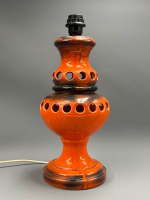 an orange ceramic lamp with holes on the base and a cord plugged into the base
