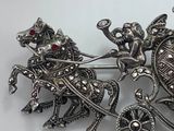a silver brooch with a horse and carriage on it