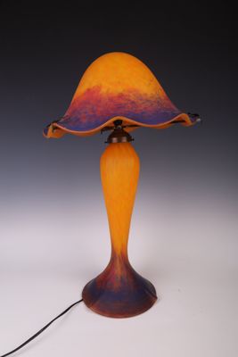 une lampe en verre orange et violet, avec un cordon noir, posée sur une surface blanche