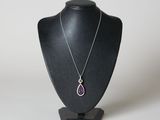 pendentif violet en forme de larme, monté sur un collier noir de type « mannequin », sur fond blanc