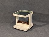 une petite table blanche avec un plateau en verre posée sur un socle gris
