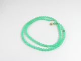 un gros plan d'un collier de perles vertes posé sur une surface blanche