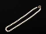 un collier de perles blanches avec un fermoir en or sur fond noir