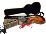 une guitare, un amplificateur et un étui à guitare posés sur une surface blanche