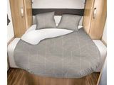 un lit avec une couette grise et des oreillers dans une petite chambre