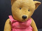 a brown teddy bear wearing a pink dress sitting on a black surface
