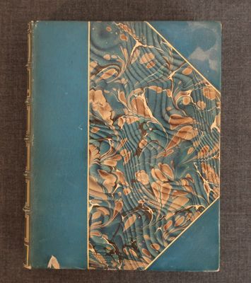un vieux livre posé sur une table recouverte d'un tissu bleu et or