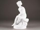 a white statue of a woman sitting on top of a rock