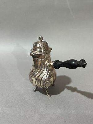 une théière ancienne en argent avec une poignée noire sur une surface blanche