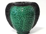 a green vase with a black handle sitting on a white surface