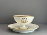 une image représentant une tasse et une soucoupe blanches ornées d'un monogramme doré