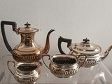 trois théières en argent et deux tasses posées sur une table en verre