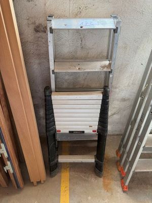 une échelle appuyée contre un mur, à côté d'une pile d'échelles