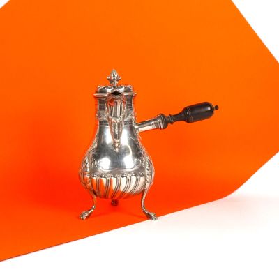une théière en argent avec une anse noire sur fond orange
