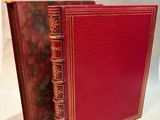an old book with a red cover sitting on top of a white surface