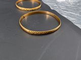 two gold bracelets sitting on top of a black surface